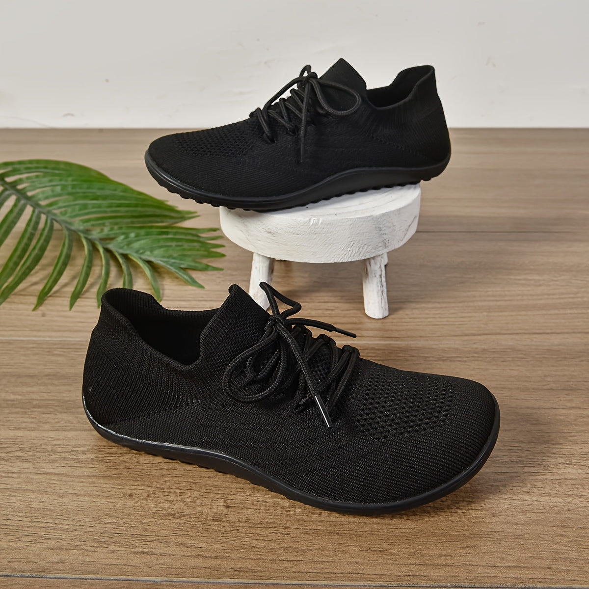 Black sneakers on a wooden surface with a white stool and green plant.